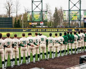 Baseball team in green and white uniforms line up along baseline at PK Park during University of Oregon game.