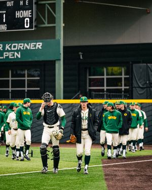 Baseball players walk off the field after a game at a stadium with green uniforms and black catcher's gear visible.