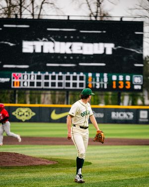 Baseball player in green and white uniform pitches on a baseball field during a game.