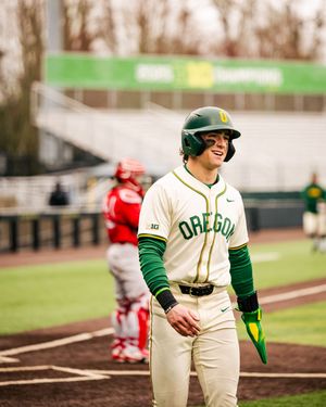 Baseball player in Oregon Ducks uniform stands ready on field during game against red-uniformed opponents.