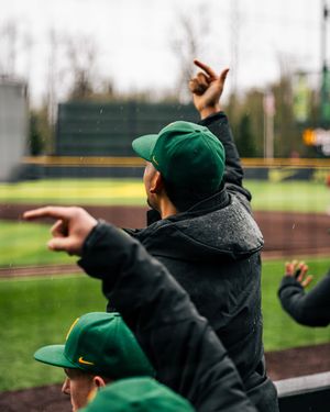 Baseball coach signals from dugout wearing green team gear and winter cap during game.