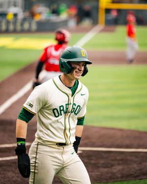 Baseball player in white and green Oregon uniform smiles while on the field during a game.