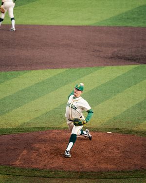 Baseball pitcher in white and green uniform winds up to throw from the mound during a game.