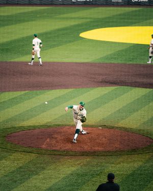 Baseball pitcher in white uniform throwing a pitch on a well-manicured baseball field during a game.