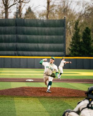 Baseball pitcher in green uniform follows through on delivery from the mound during a game on a well-manicured field.