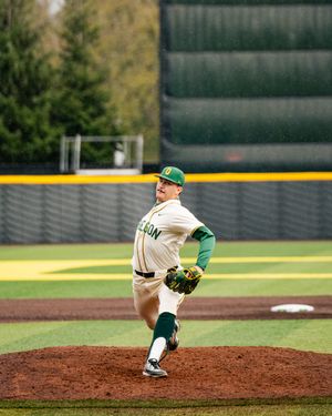 Baseball pitcher follows through on delivery from the pitcher's mound in green and white uniform.