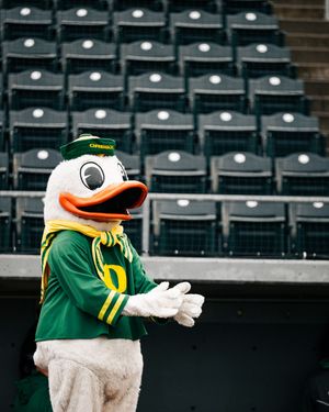 Oregon Ducks mascot in green jersey gestures while standing in front of empty stadium seats.