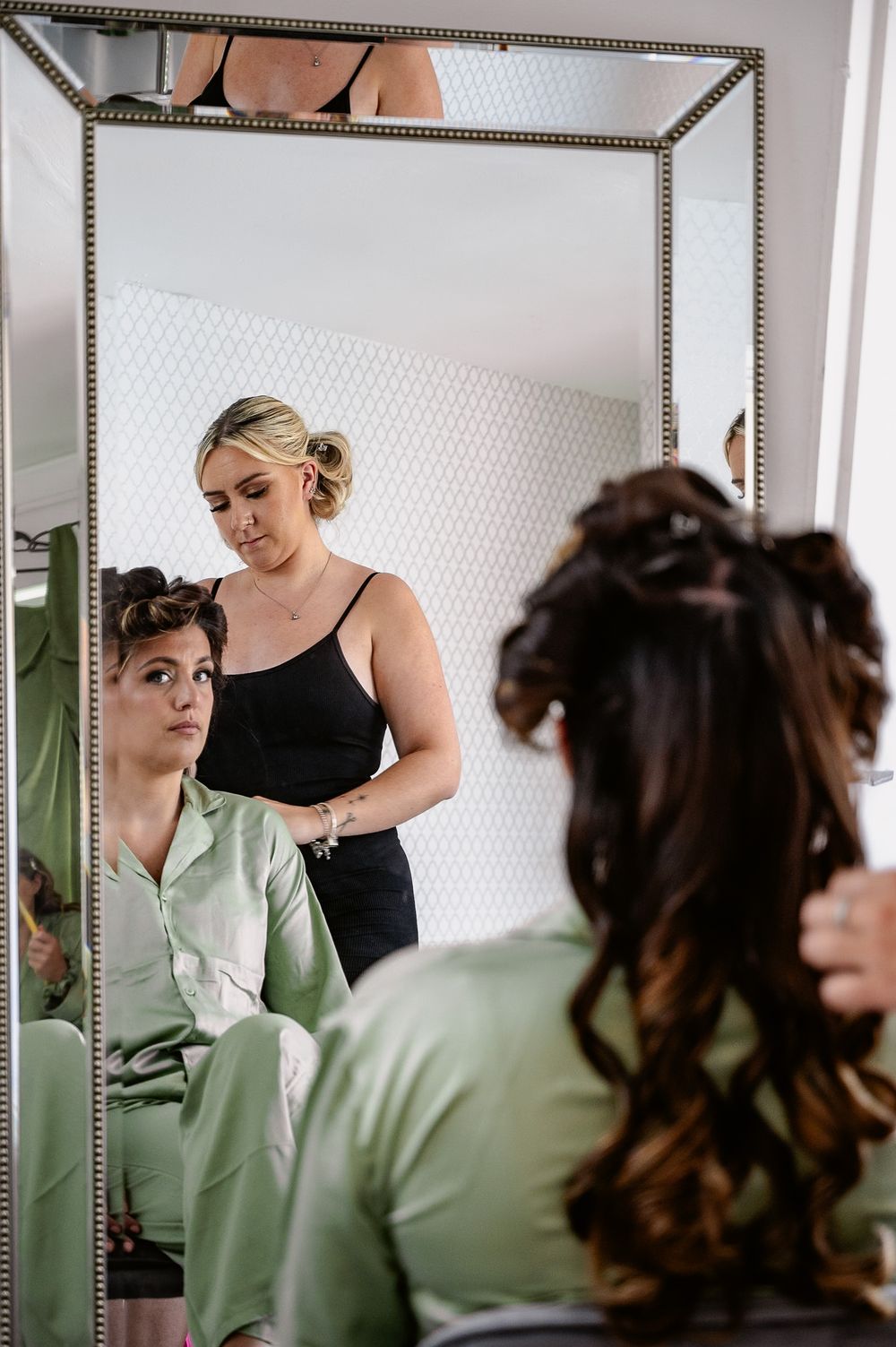 Bridesmaids in mint green dresses getting ready in front of a framed mirror.