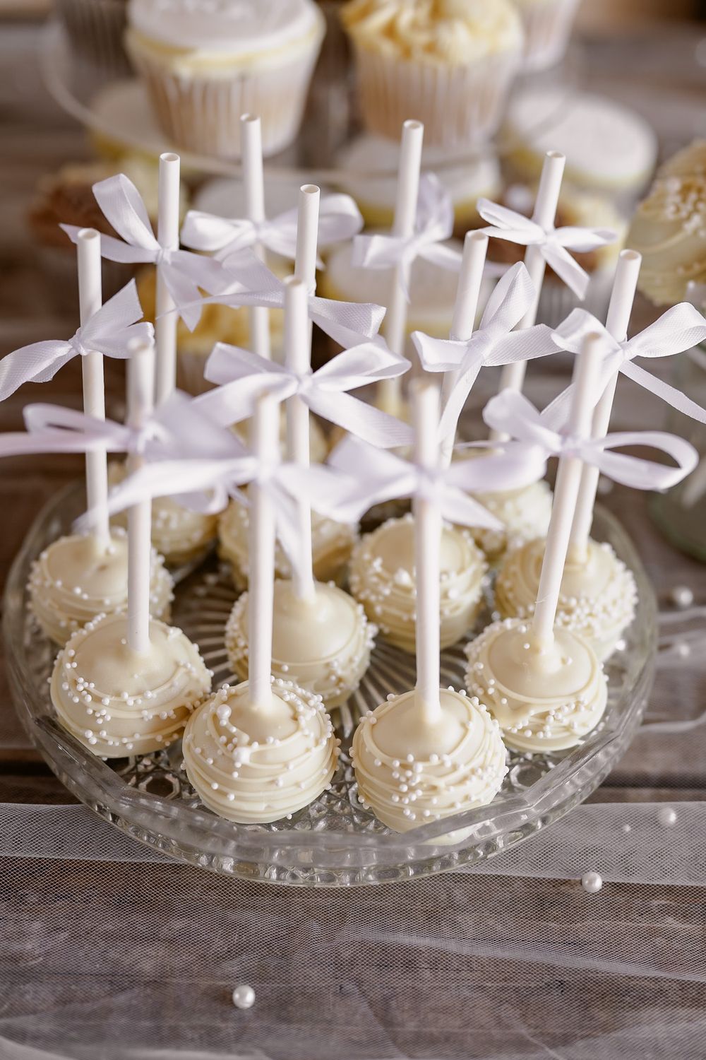 White chocolate cake pops decorated with bows arranged on clear display plates.