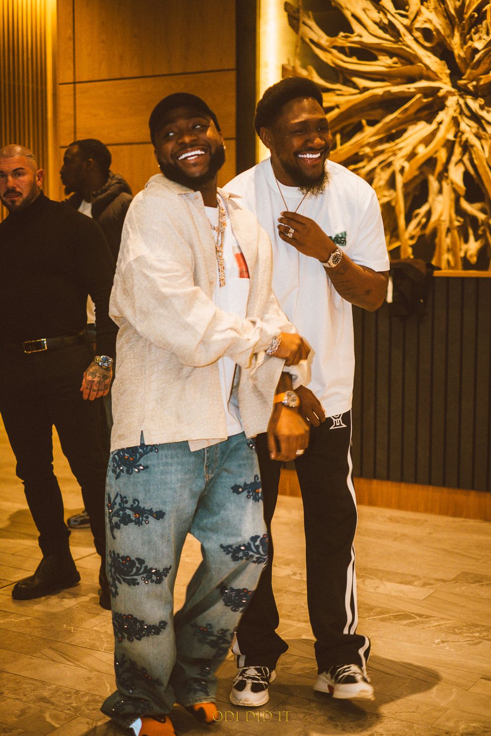 Two friends share a joyful moment laughing together in a warmly lit hallway with decorative wall art.