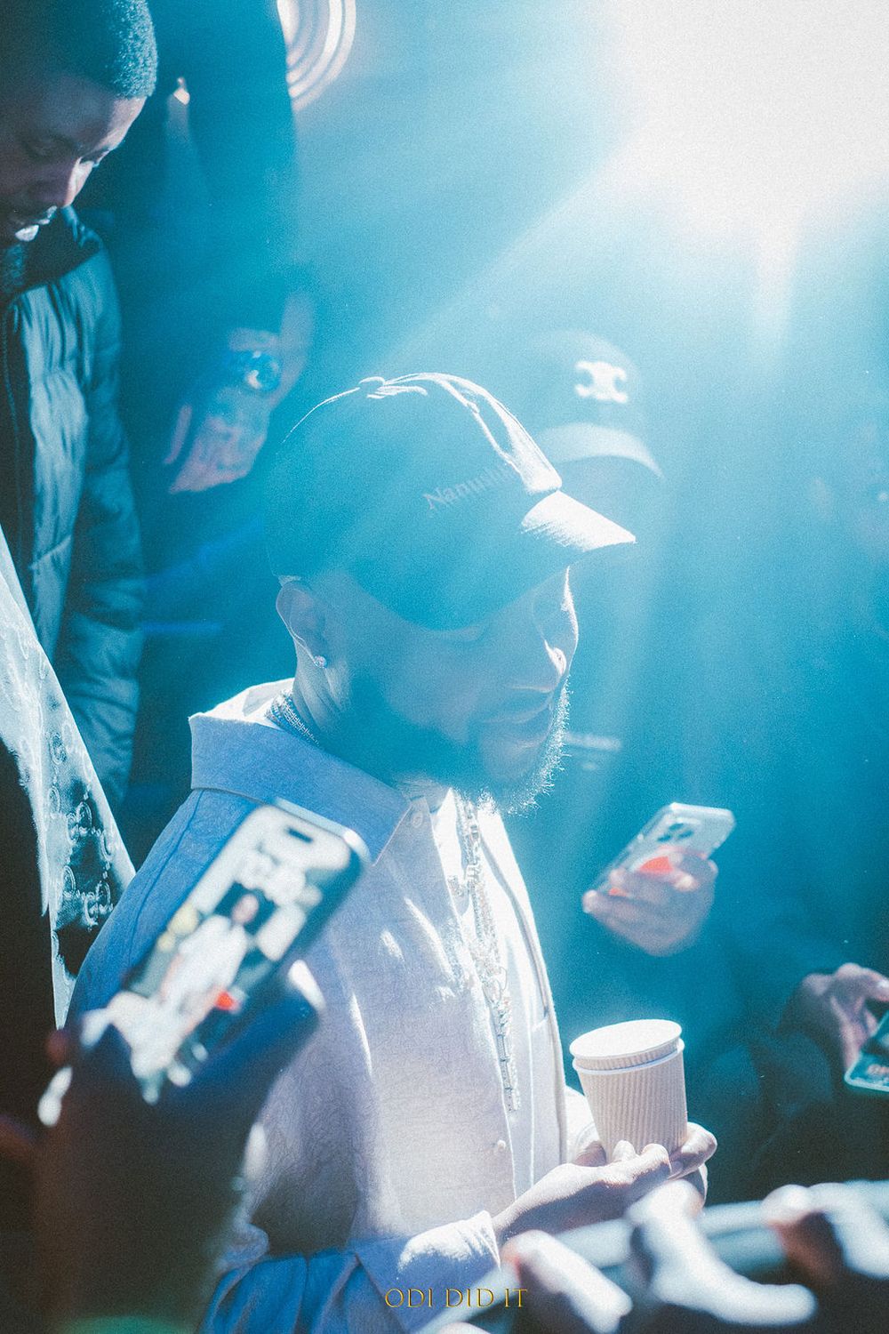 People checking their phones in a crowded space with blue atmospheric lighting and a coffee cup visible.