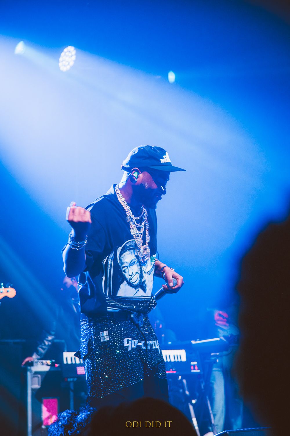 A performer in dark clothing and a hat silhouetted against dramatic blue stage lighting during a concert performance.