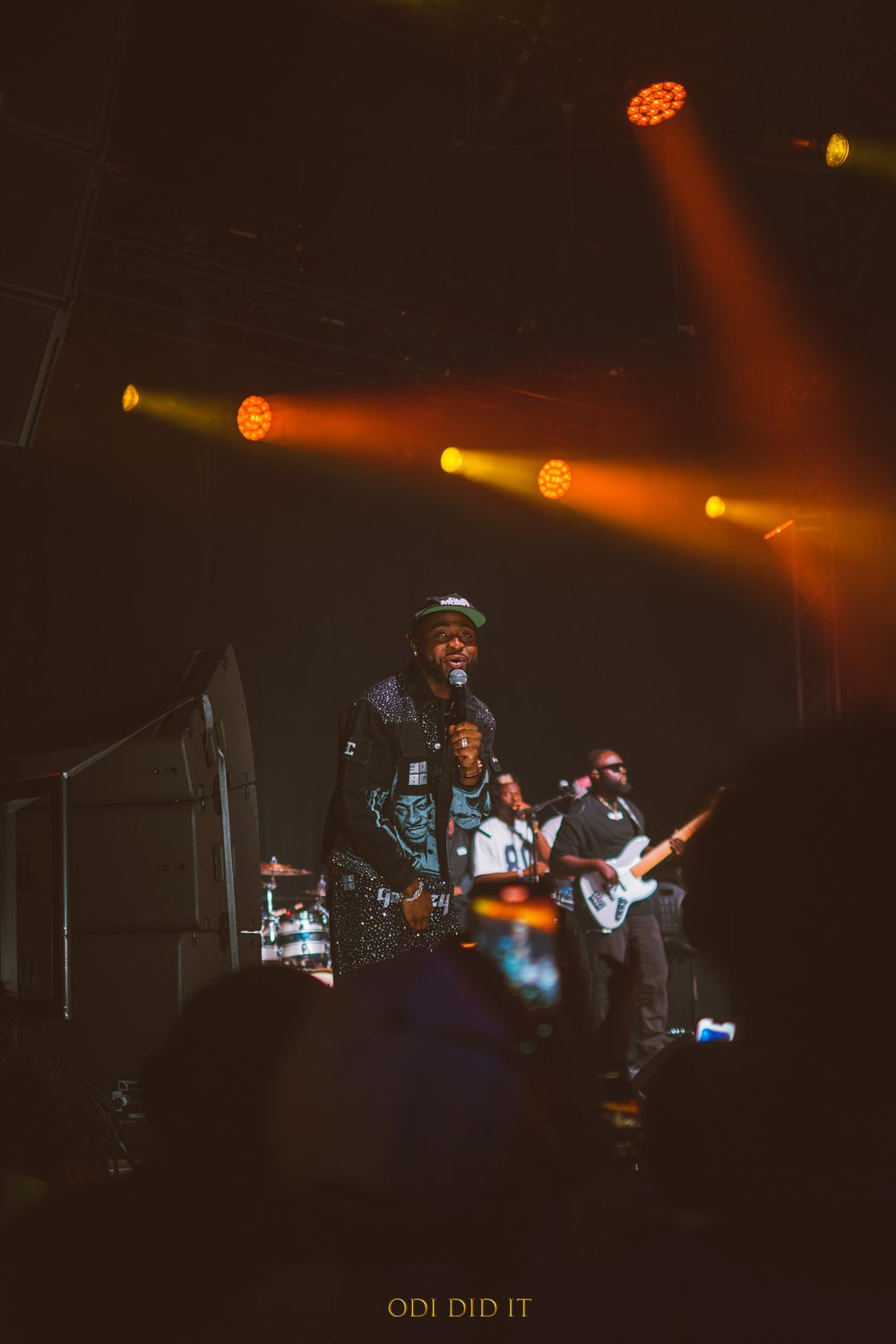 Musicians perform on a dimly lit stage with dramatic orange lighting and spotlights creating an atmospheric concert scene.