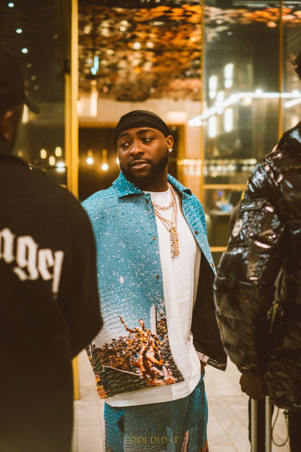 Person wearing sparkly blue jacket and white shirt poses at night with city lights in background.