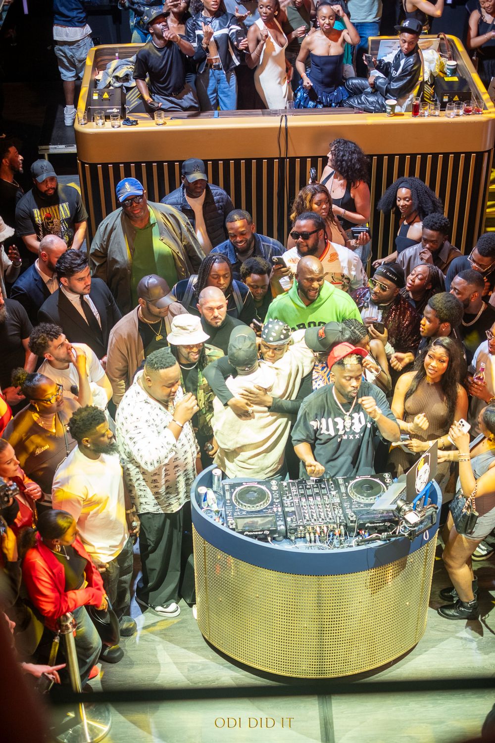 A crowd of people gathered around a circular display table examining items in what appears to be a retail setting.