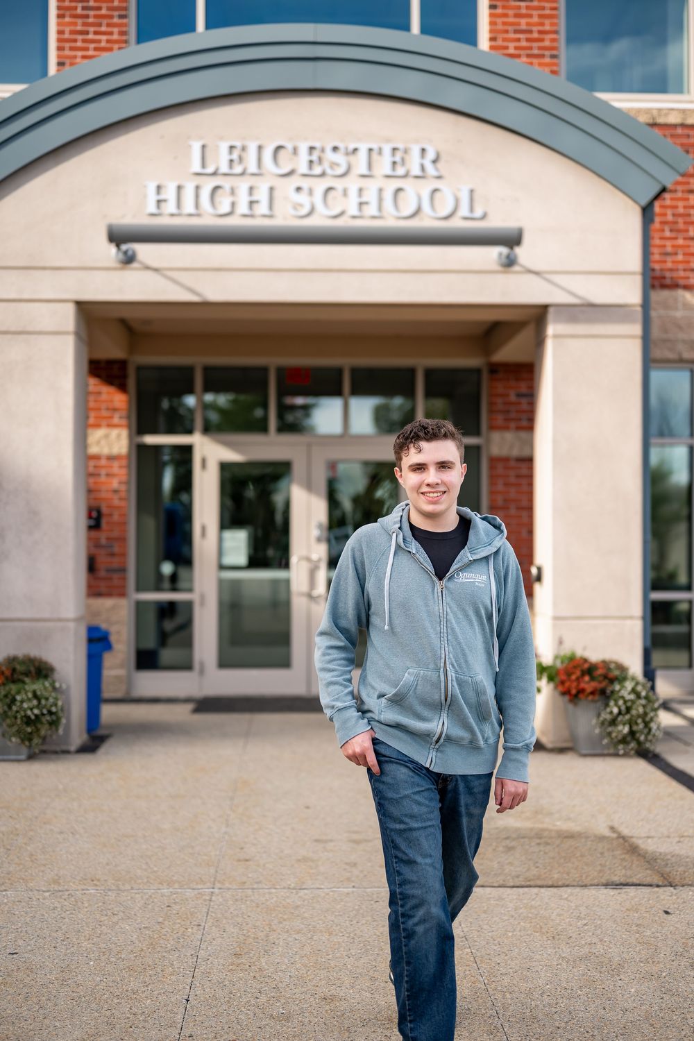 Student in casual attire stands in front of Leicester High School entrance on an autumn day.