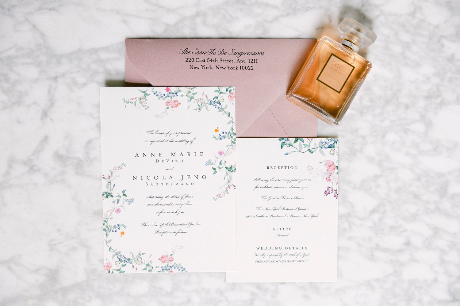 Wedding invitation suite featuring blush pink and floral designs displayed on a white marble background with gold accents.