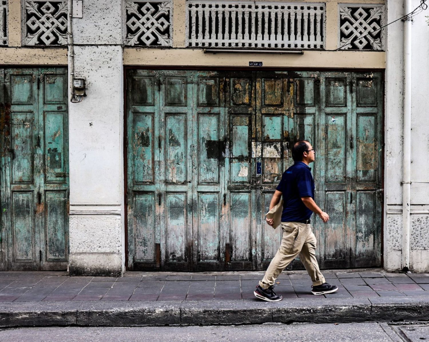 Person walking past a weathered teal wooden storefront on an urban street.