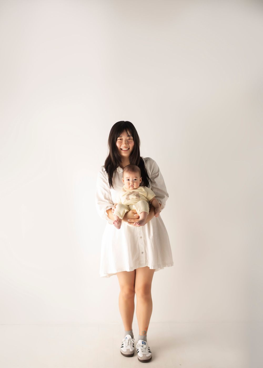 Studio portraits showing mother and baby in white outfits against light background.