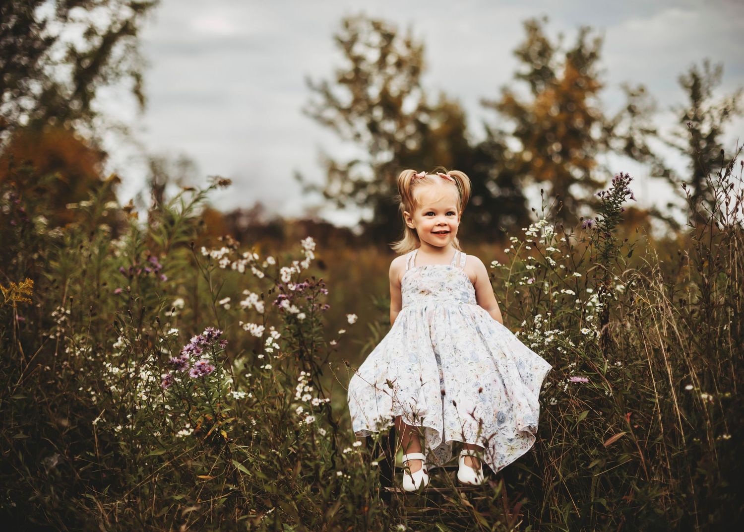 Child in white dress playing in field during golden hour.