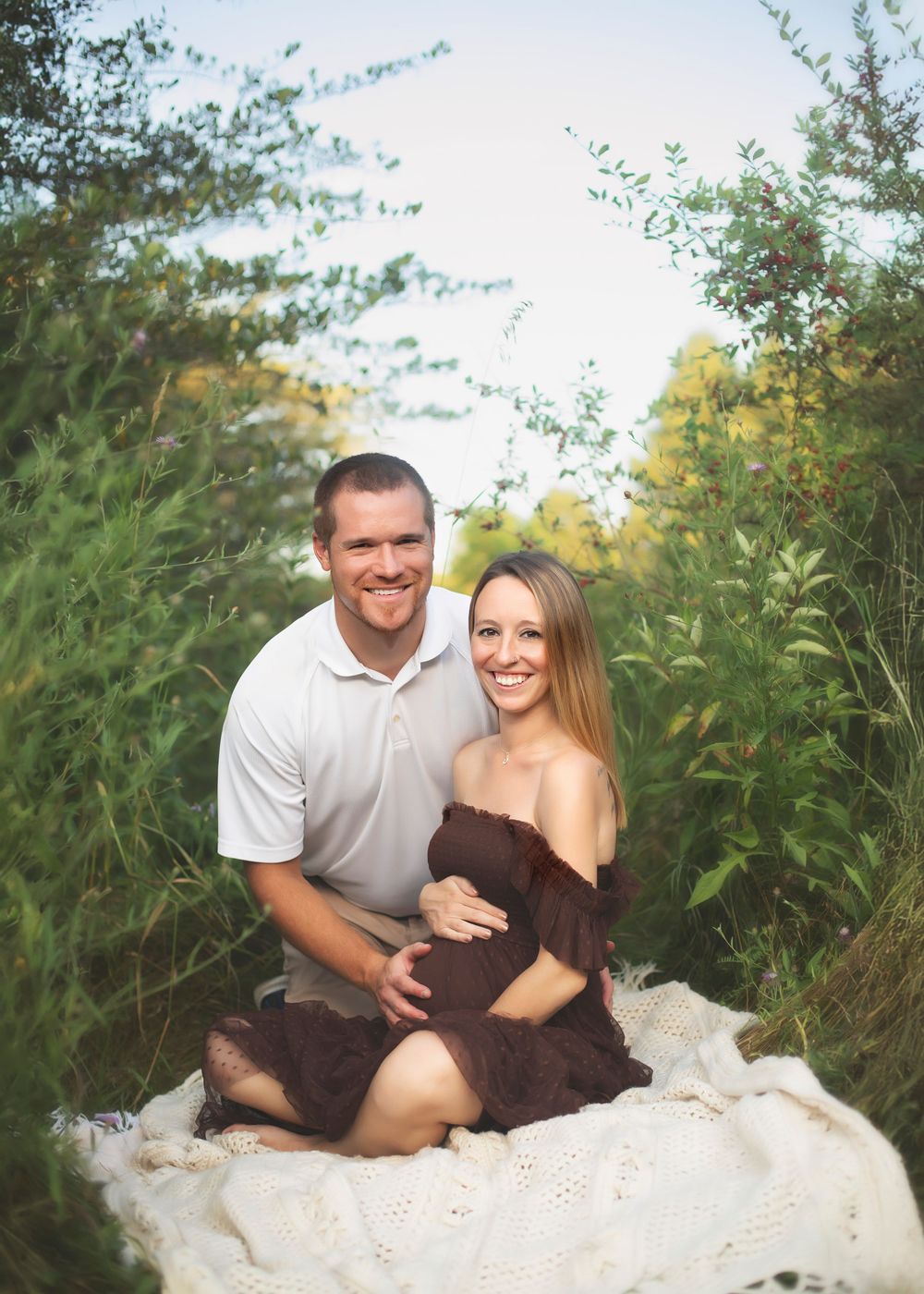 Maternity photo series of couple sitting together outdoors among tall green plants.