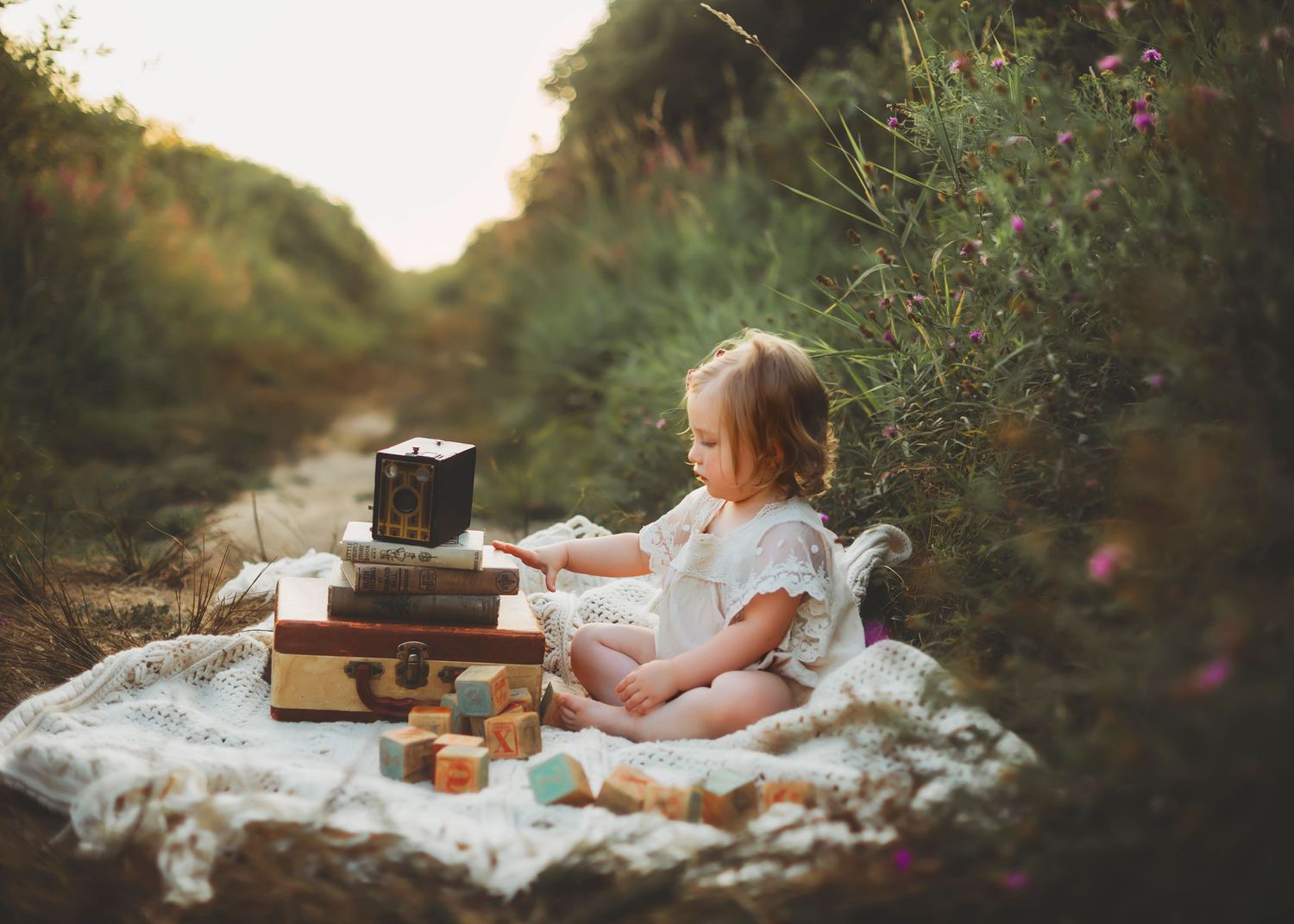 A vintage picnic scene at sunset with white lace blankets, wooden crates, and soft glowing light through trees.