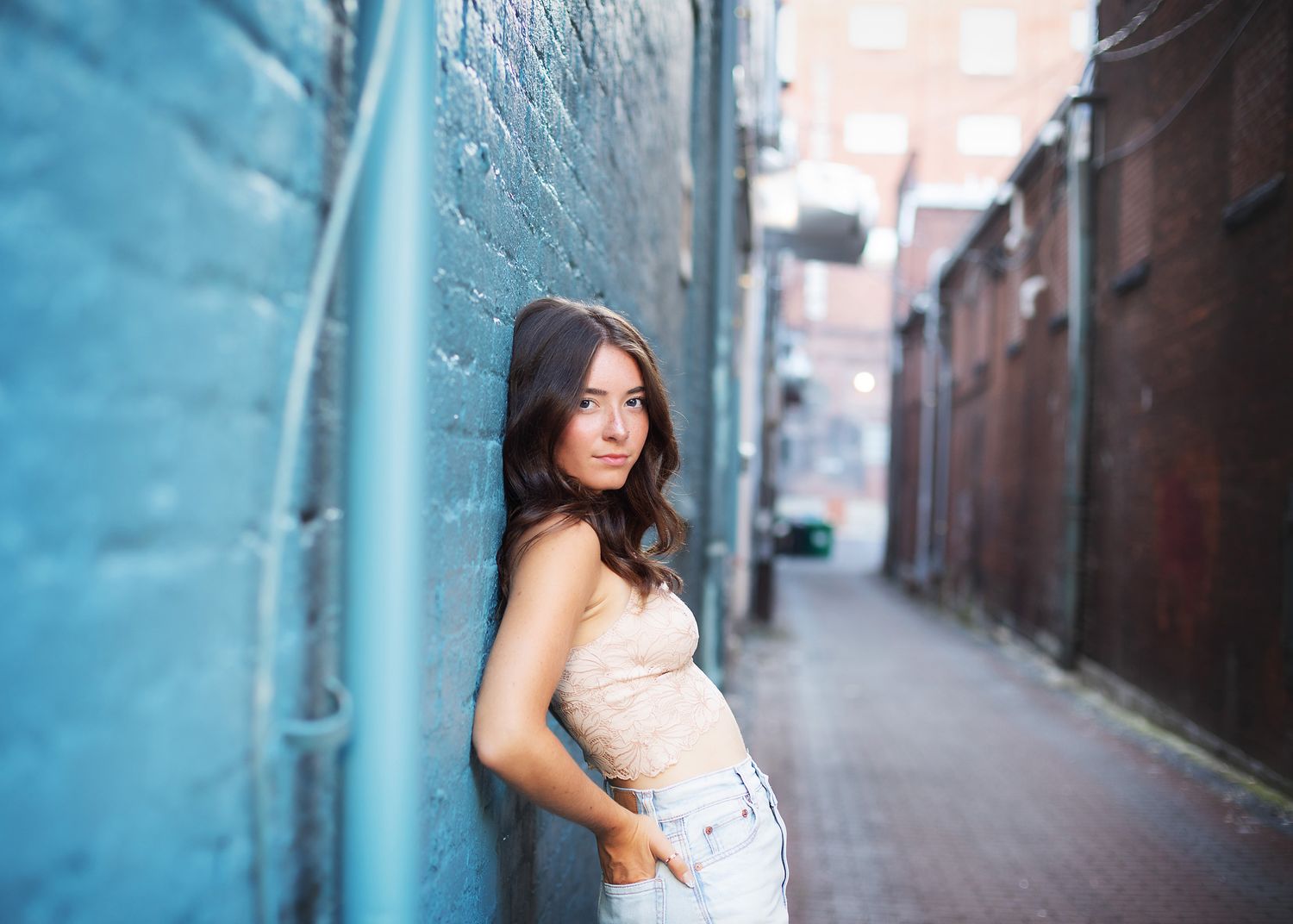 Urban portrait session against blue wall in historic brick alleyway.
