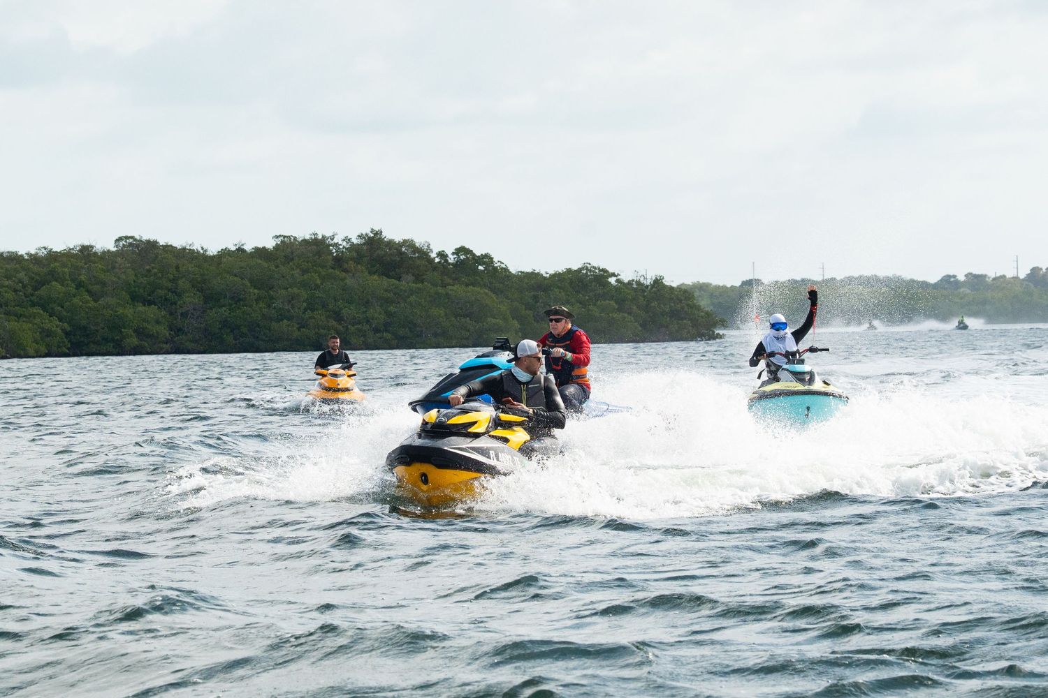 Group of jet skiers racing across choppy waters on colorful watercraft, creating white wakes behind them.