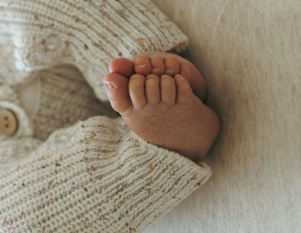 A tiny baby foot rests against a cozy white knitted blanket in a gentle, heartwarming close-up shot.
