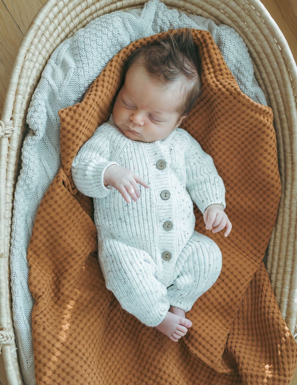 Baby in white knit sweater lying on brown waffle textured blanket viewed from above.