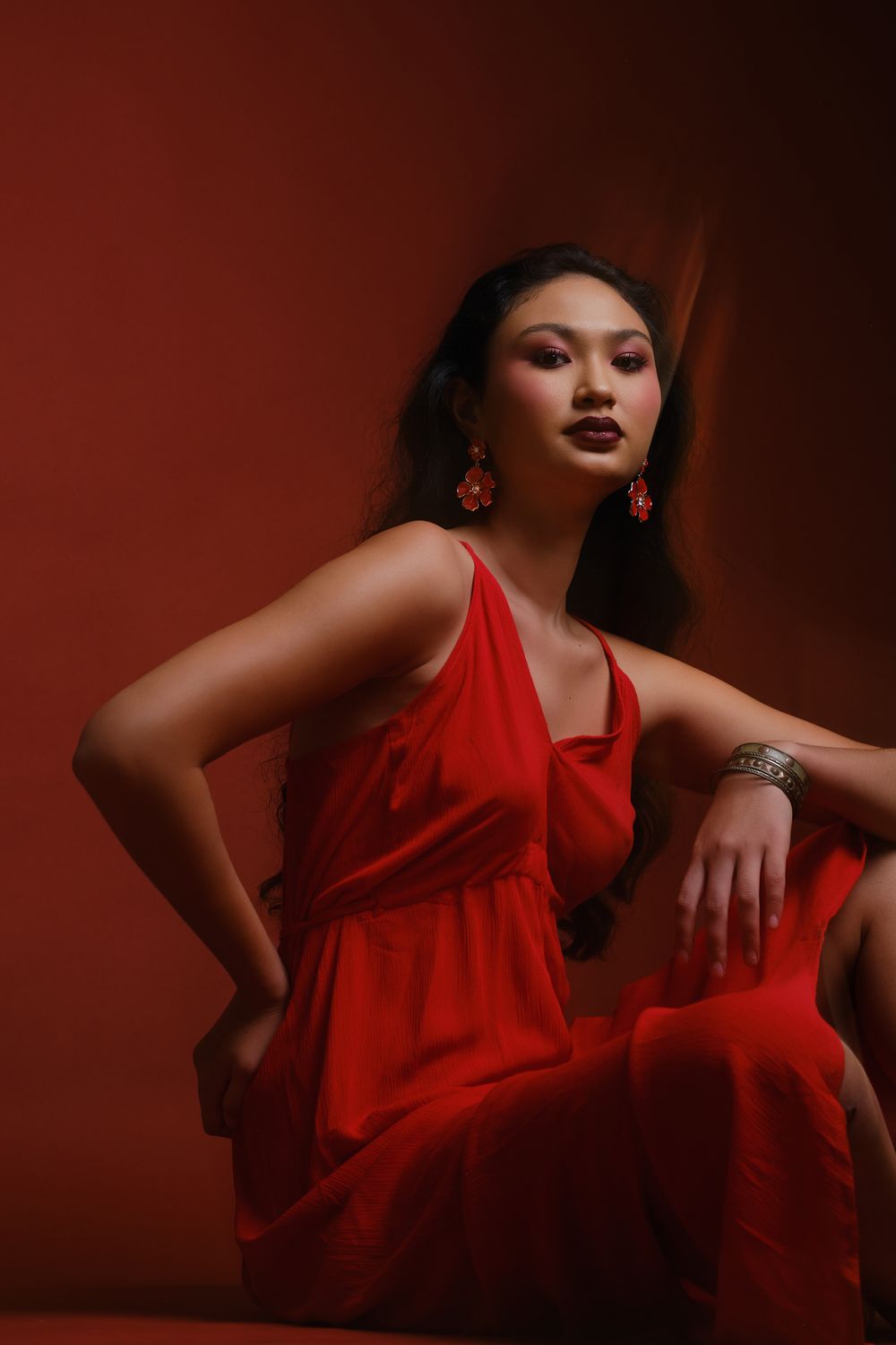 Hiilei, modèle de la Tahiti Fashion Week, assise au sol, en robe rouge, sur un fond rouge, en studio.
