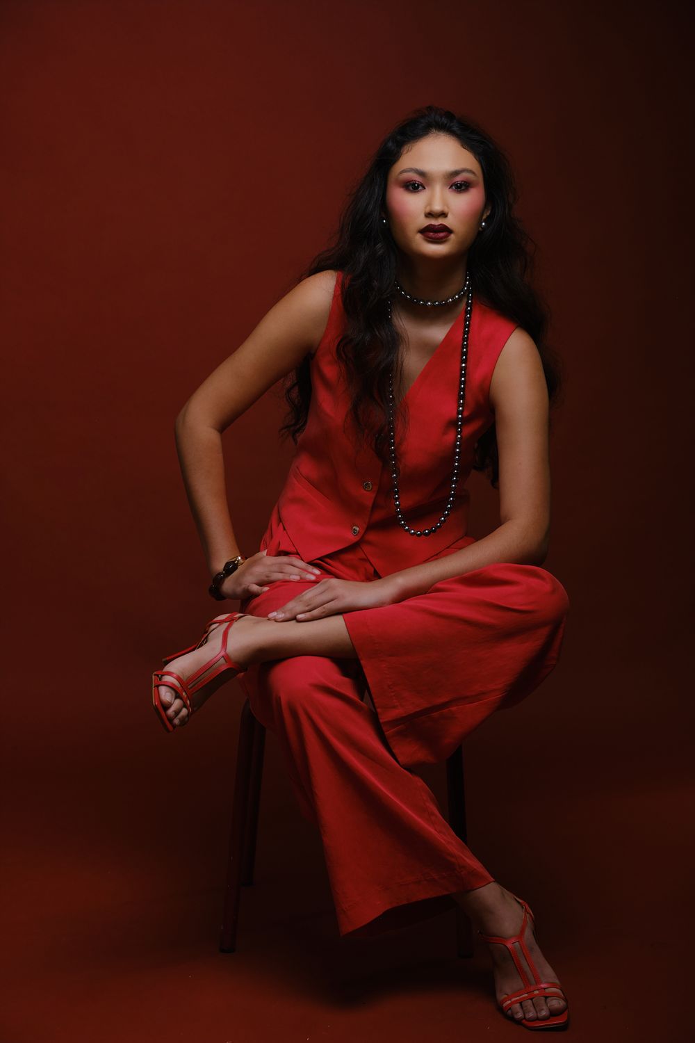 Hiilei, modèle de la Tahiti Fashion Week, assise sur un tabouret, les jambes croisées, sur un fond rouge, en studio.