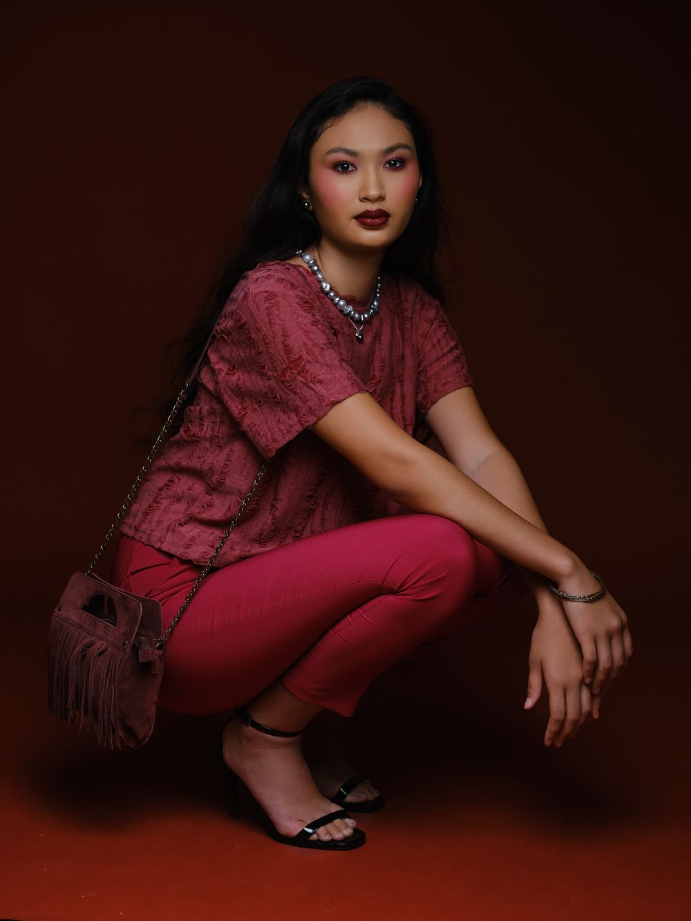 Hiilei, modèle de la Tahiti Fashion Week, posant accroupie sur un fond rouge en studio.