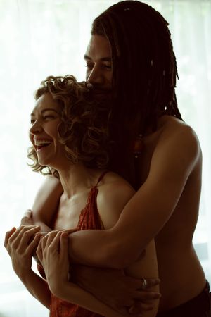 Backlit couple sharing a tender moment and laughing together against bright window light.