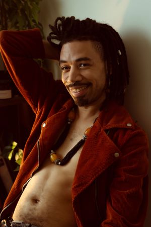 Person in red corduroy jacket smiling warmly in moody indoor lighting with dreadlocks.