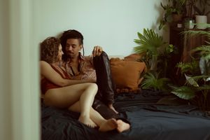 a couple lounging on a dark couch with potted plants in the background of a dimly lit room.