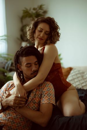 A couple embraces intimately in a warm-toned room with soft lighting and natural window light.