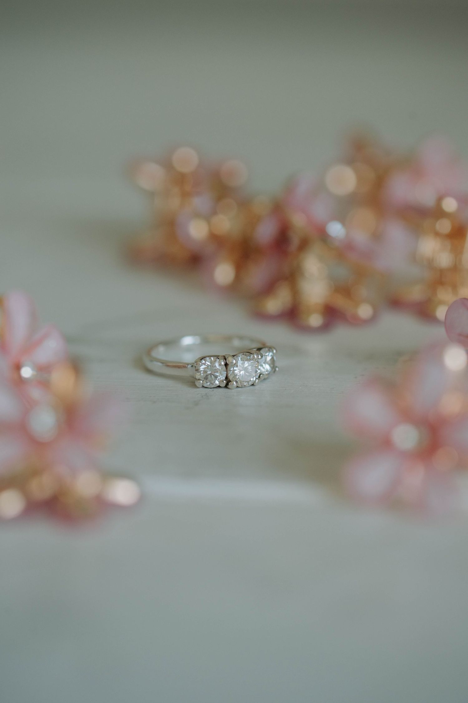 A delicate diamond engagement ring sparkles against a soft background with blurred pink and gold bokeh lights.