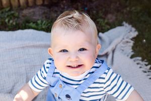 Adorable baby in striped nautical outfit smiling during outdoor photoshoot.