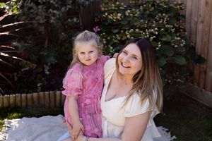 A joyful outdoor photoshoot with a pink-dressed child and adult against a wooden fence background.