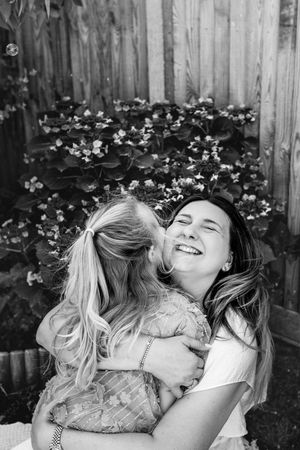 A black and white candid photo capturing a loving embrace outdoors with flowers in the background.
