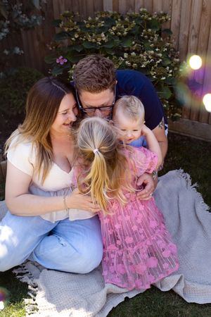 Family sitting together on a blanket in backyard with string lights and wooden fence.