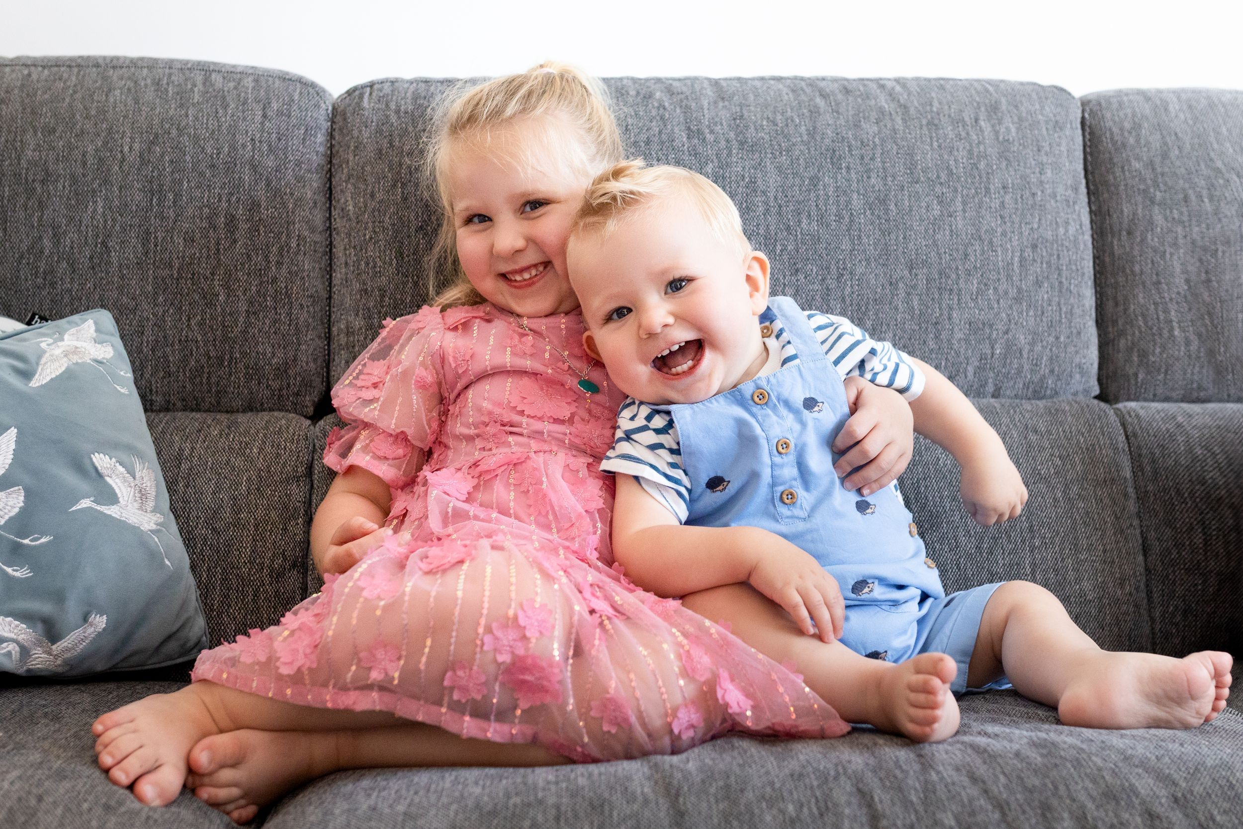 A family relaxes together on a grey couch with decorative throw pillows.