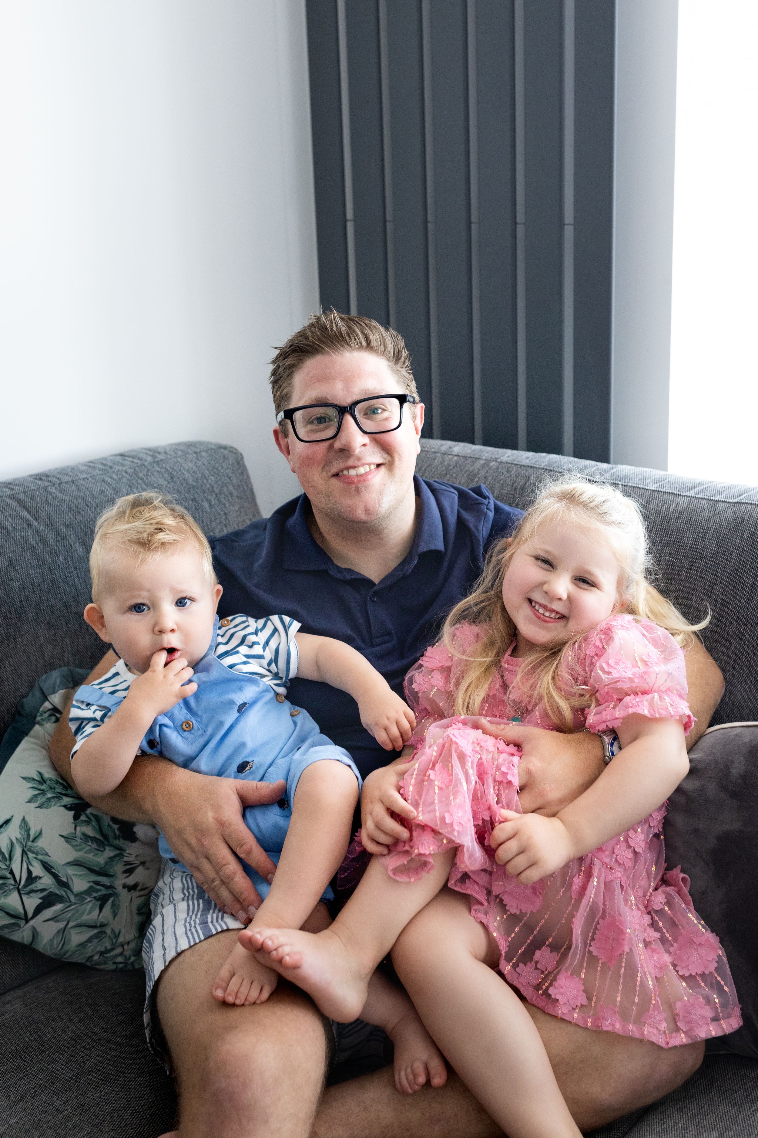 Family cuddles together on a gray couch in a series of playful poses.