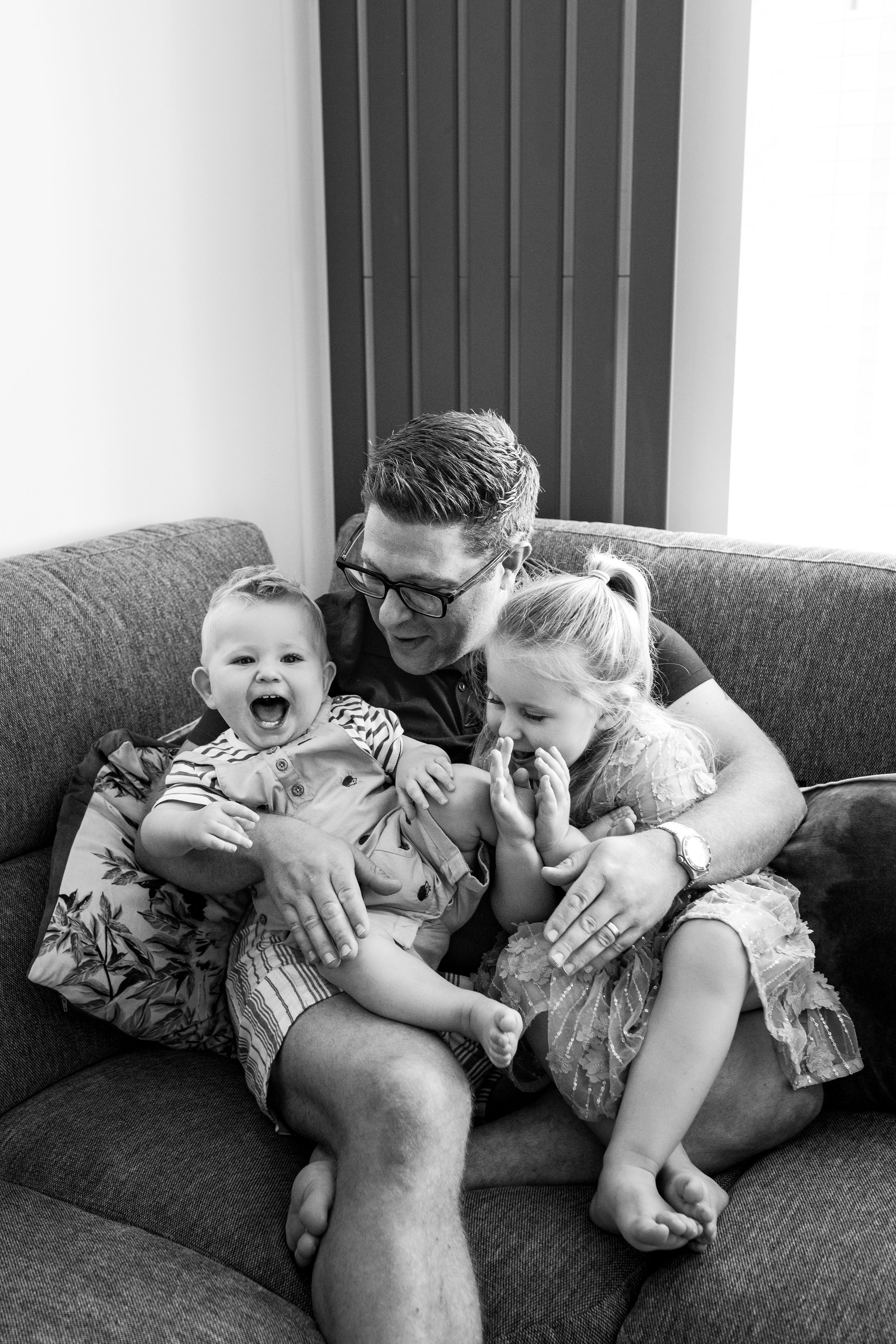Series of black and white photos showing playful moments on a couch with expressions of joy and laughter.