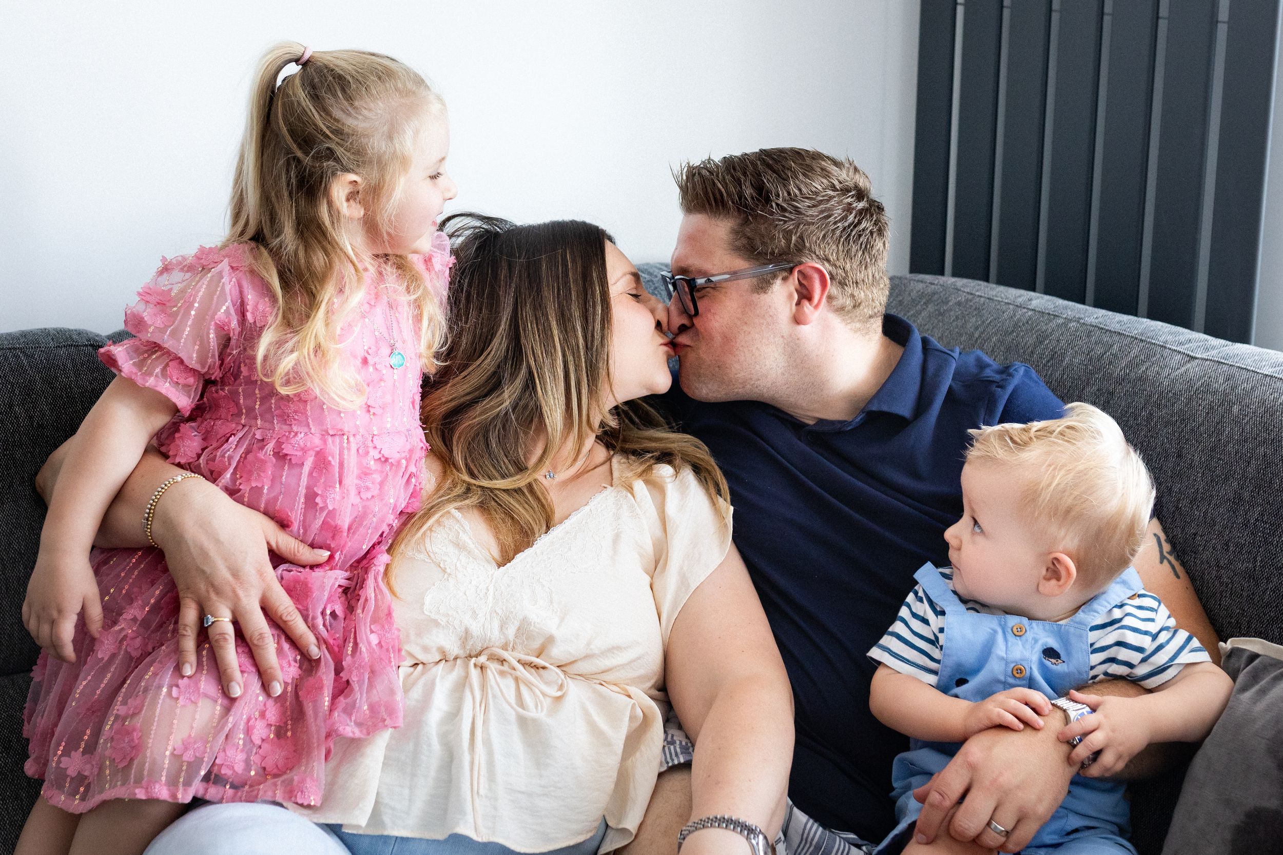 Family enjoying tender moments together on a cozy couch during an indoor photoshoot.