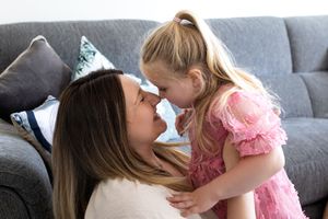 A tender moment of affection shared between parent and child on a gray couch in natural lighting.
