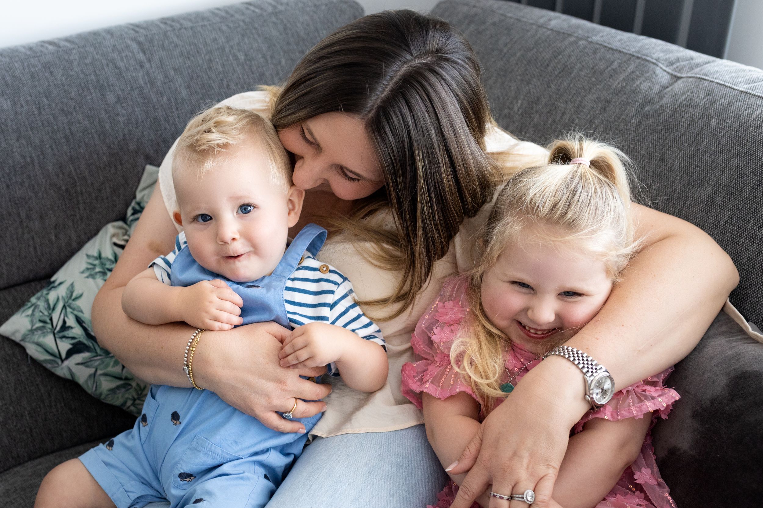 A tender family moment on a gray couch as three people snuggle close together in a warm embrace.