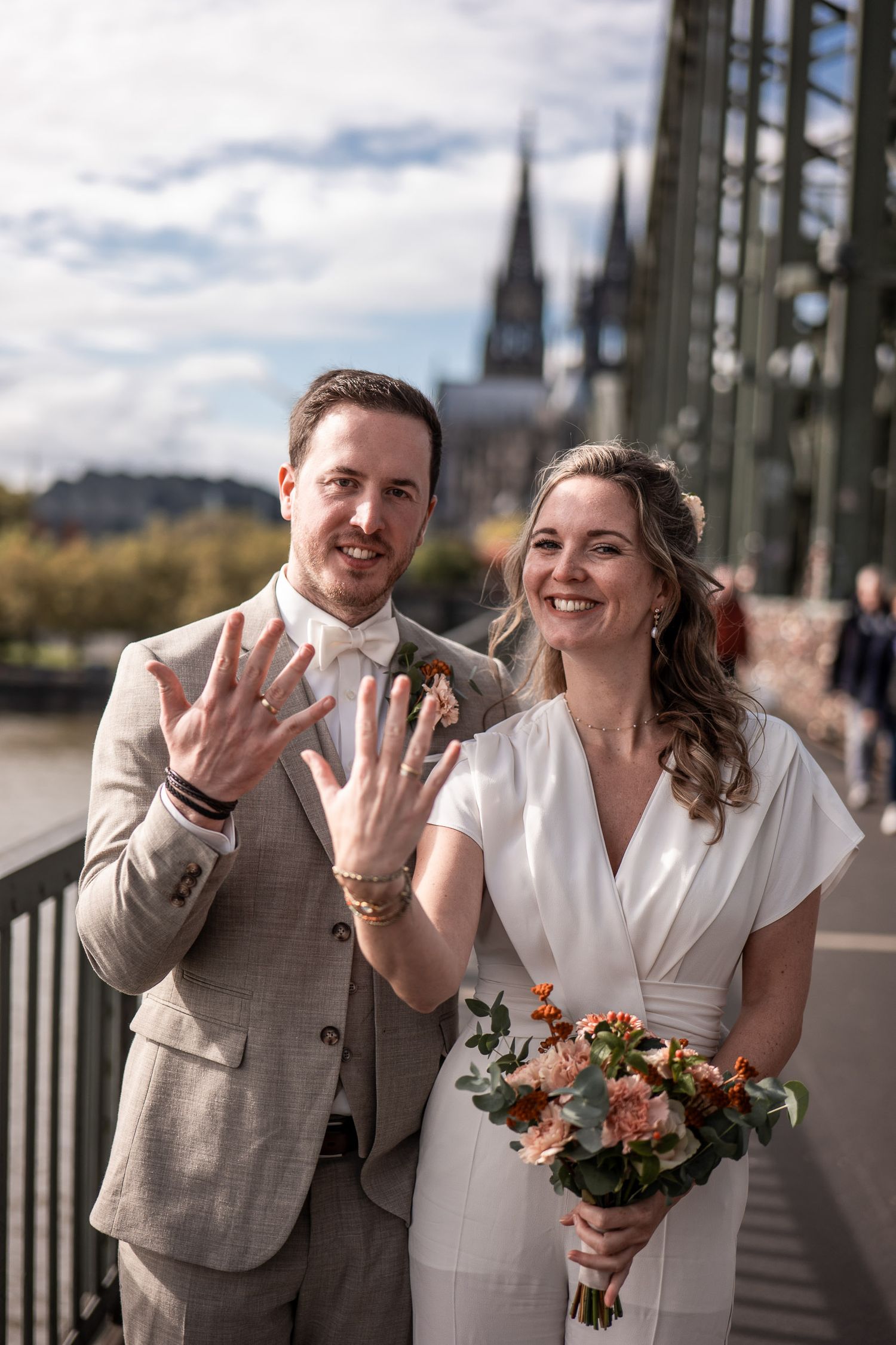 Glückliches Brautpaar zeigt lächelnd die Eheringe während einer urbanen Hochzeit in Köln.
