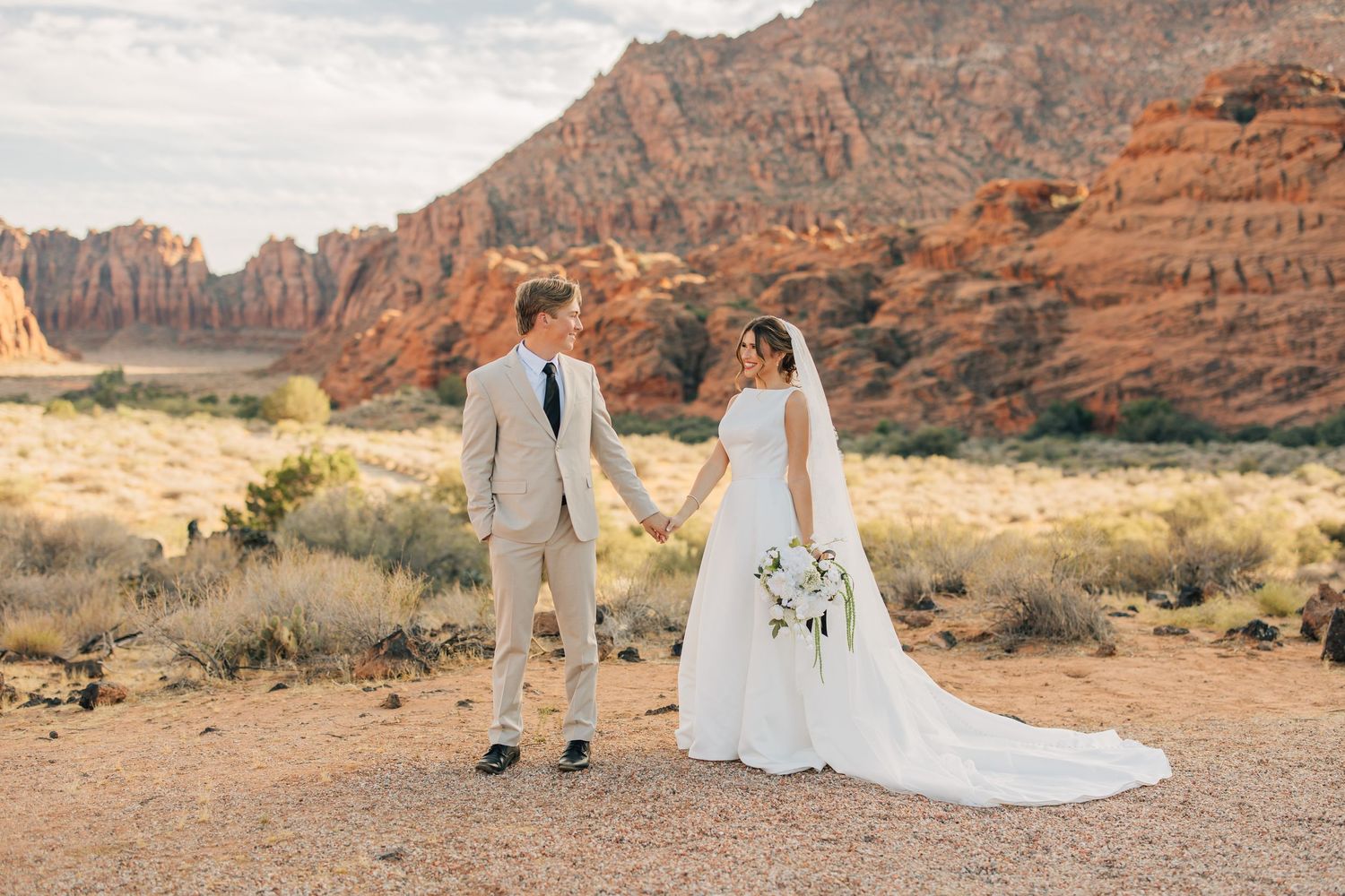 A couple embraces during their desert wedding ceremony at sunset with red rock formations in Snow Canyon State Park, Utah.
